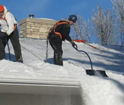 Professional technicians performing roof snow removal with safety harnesses and shovels in {city}, {state}
